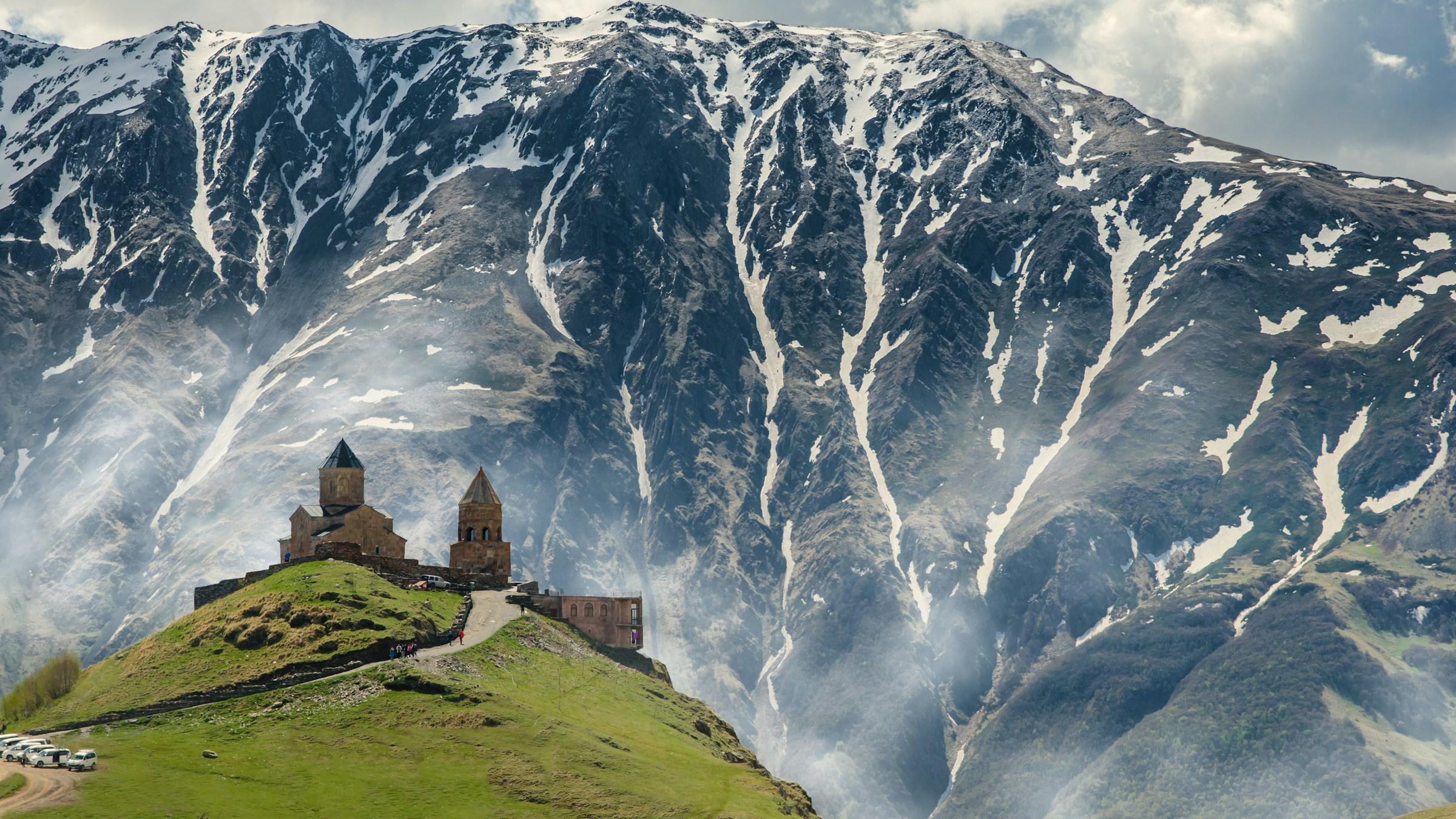 Gergeti Trinity Church on its hill above Stepantsminda, with snowy Caucasus slopes behind
