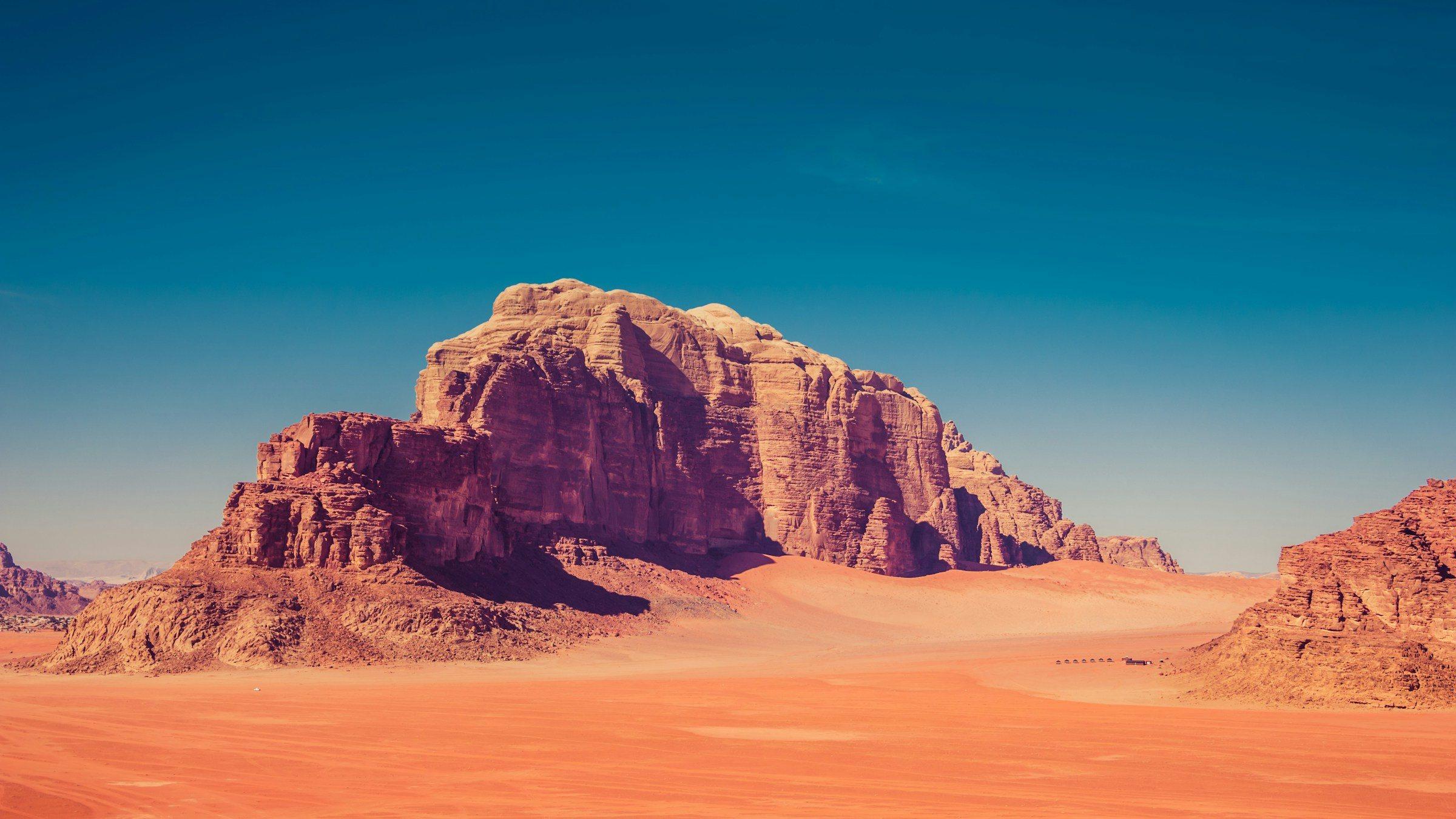 A sandstone massif rising from red sand in Wadi Rum, Jordan