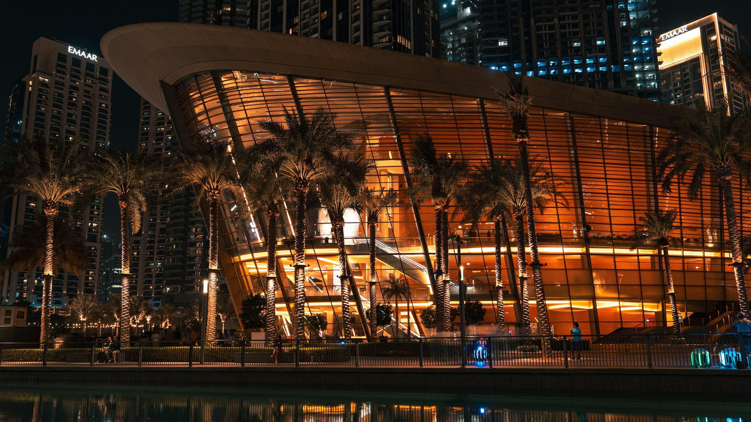 Dubai Opera lit up at night among palms and Downtown towers