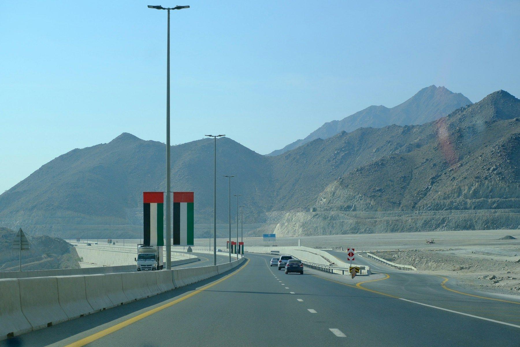 A highway through the Hajar Mountains past a monument in the colours of the UAE flag
