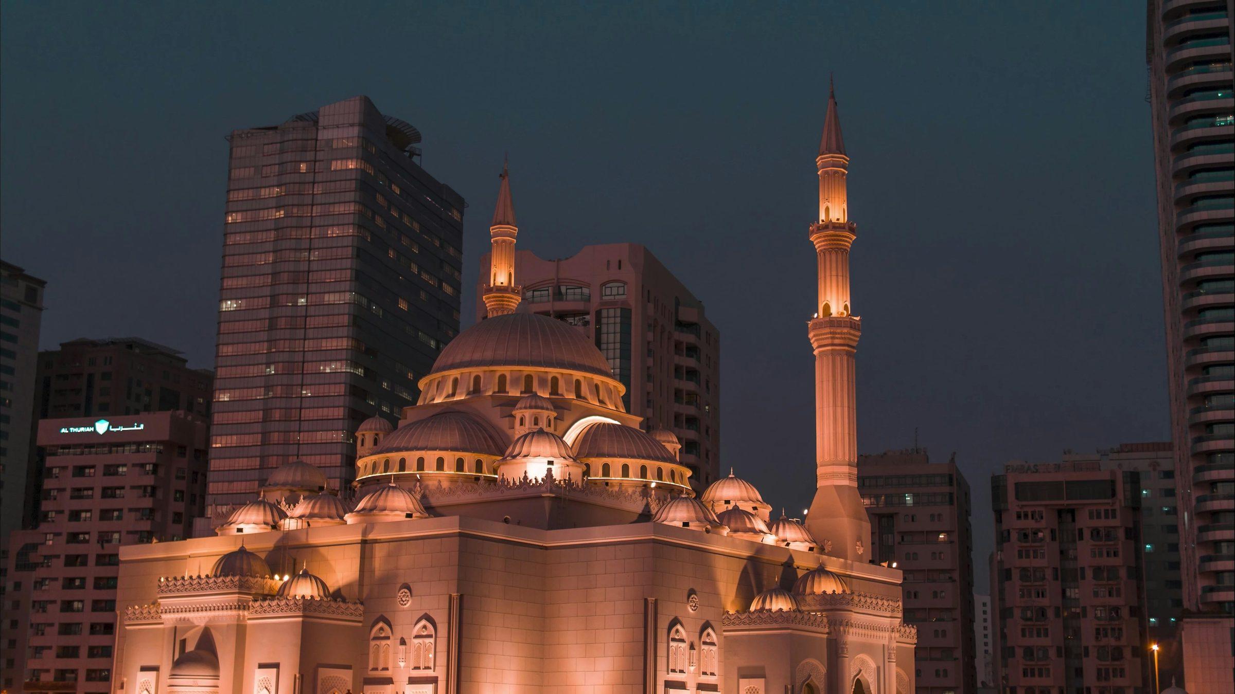 Al Noor Mosque lit up at dusk among the towers of Sharjah
