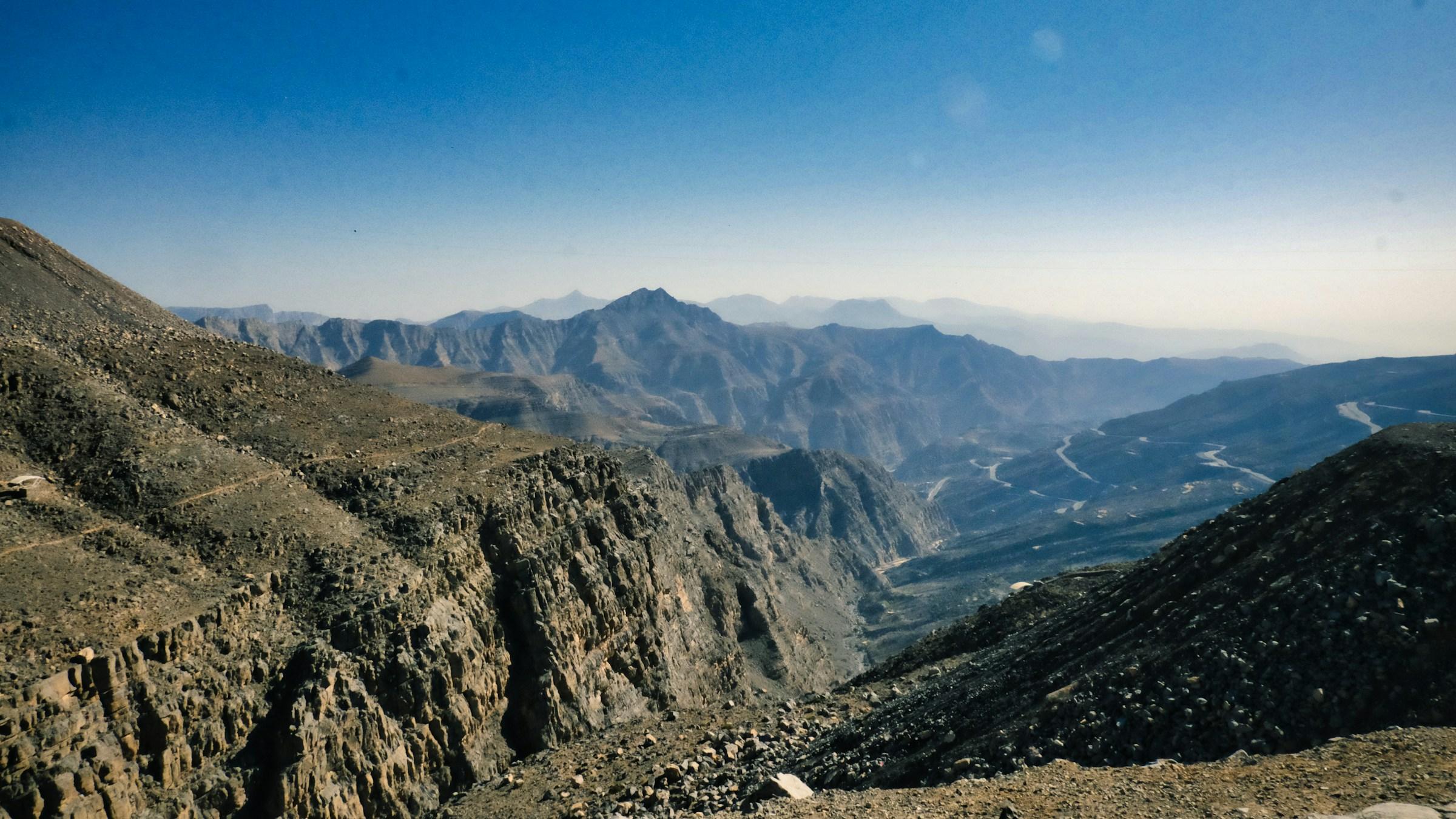 Jagged ridges of the Hajar Mountains seen from high on Jebel Jais, with the road winding through the valley below