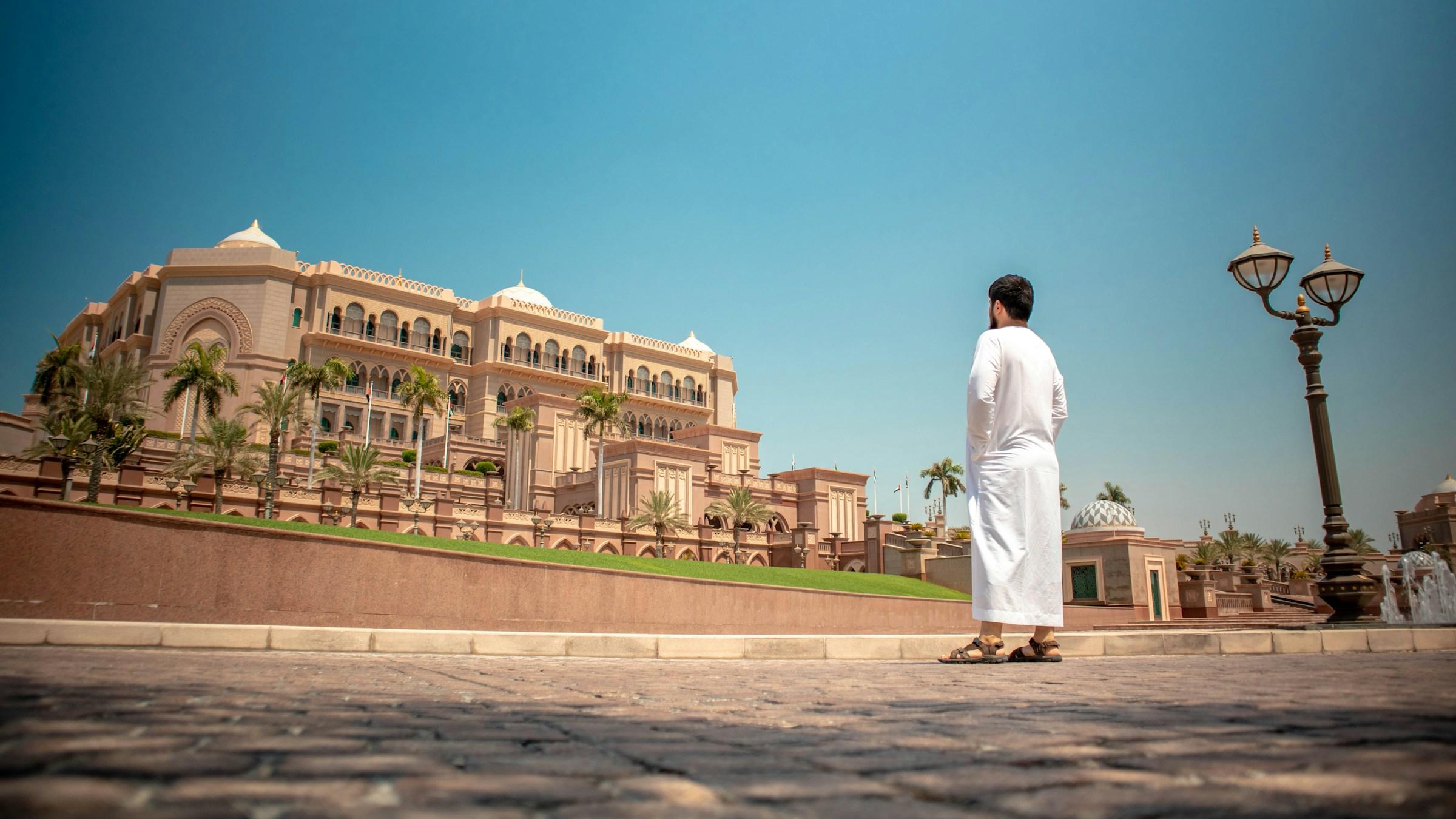 A man in white robes looking out at Emirates Palace in Abu Dhabi