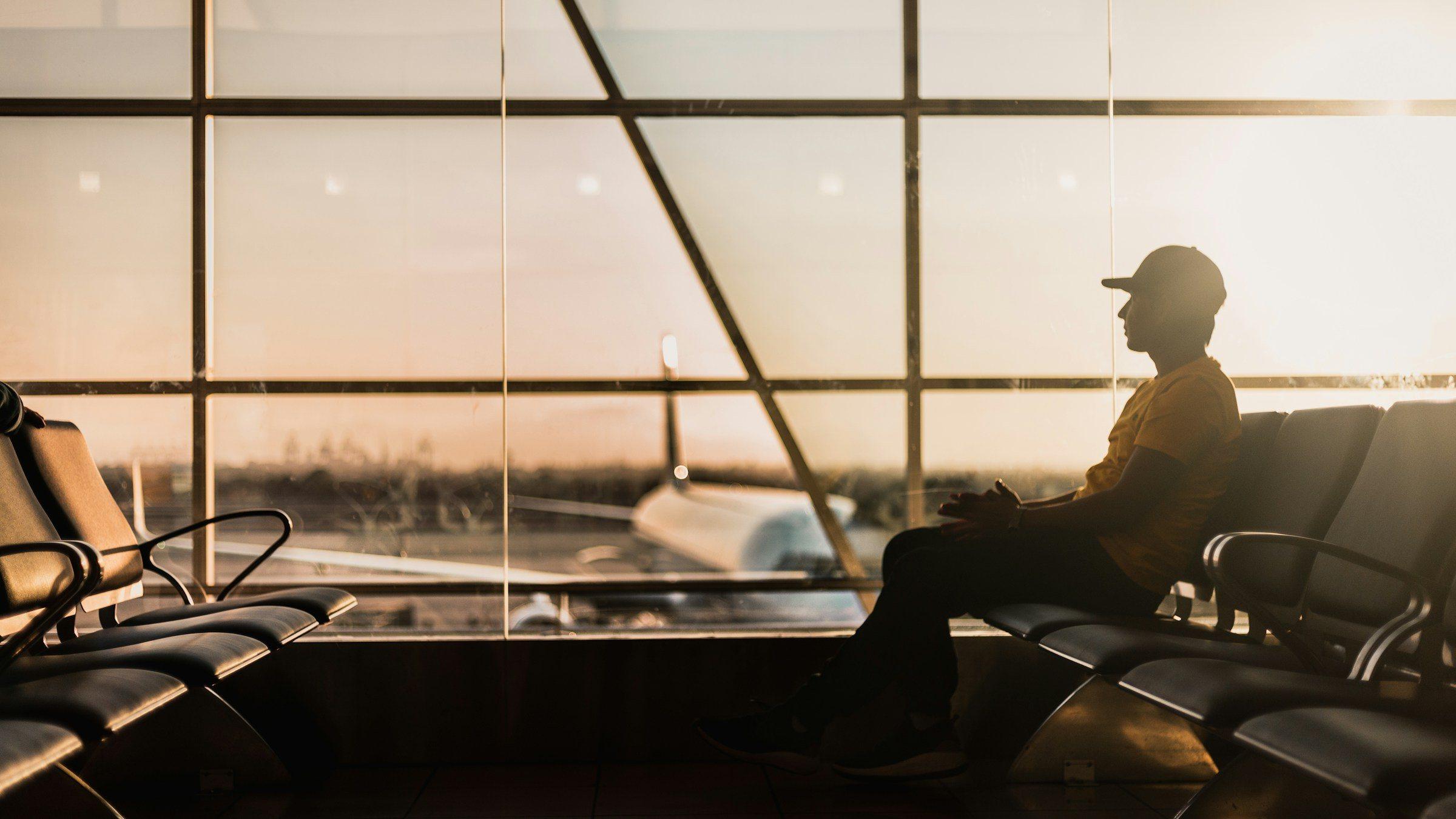 A traveller waiting by the terminal window as the sun sets over the apron