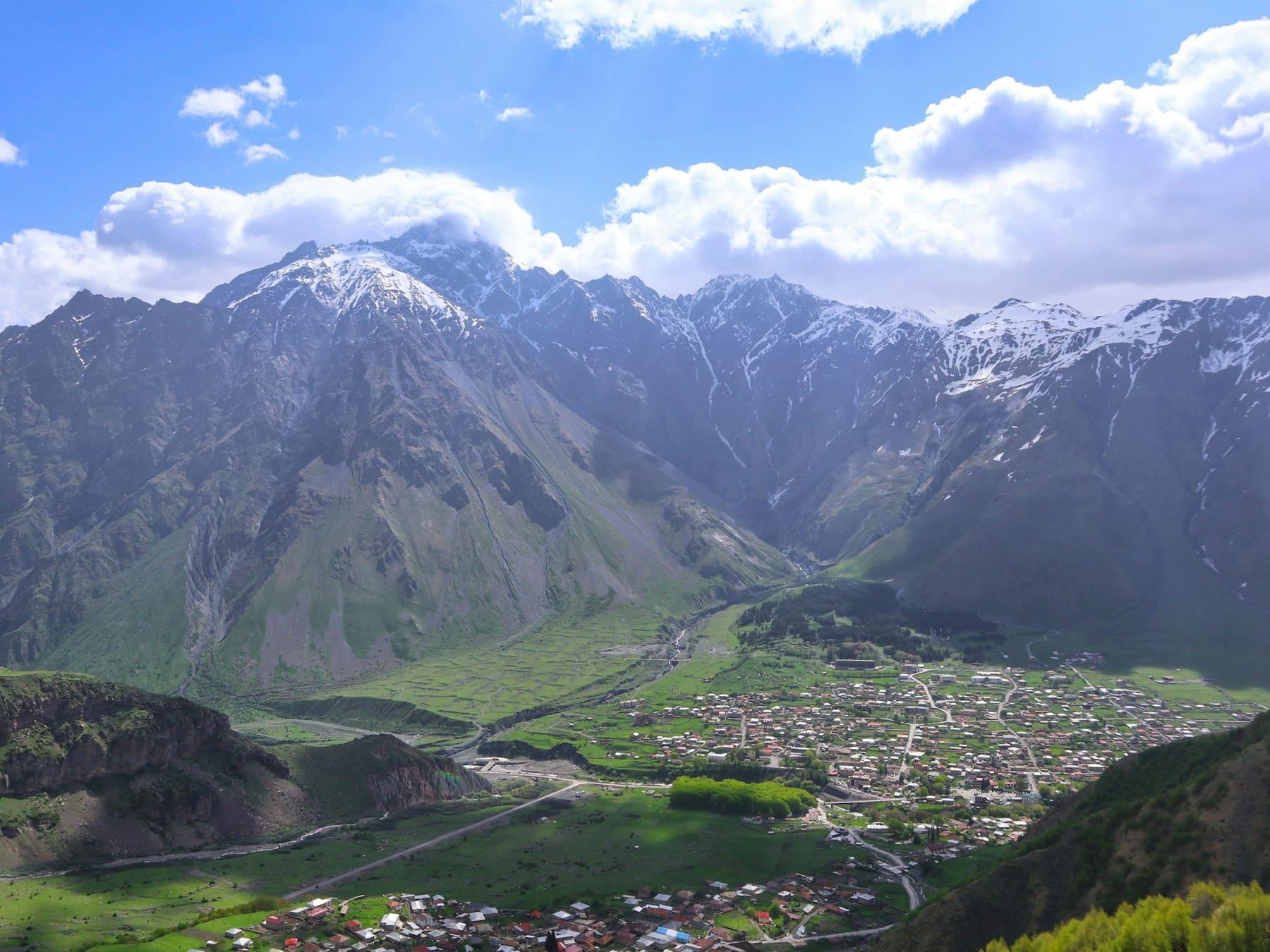Stepantsminda in its green valley below the snow-capped Caucasus, Kazbegi