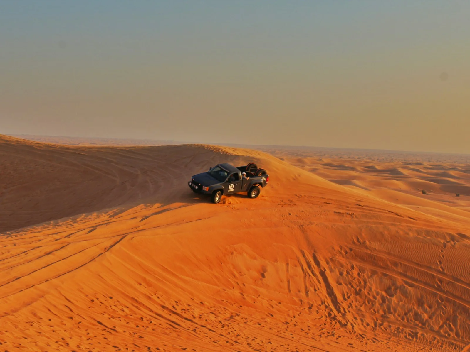 سيارة دفع رباعي (4x4) على حافة كثيب في صحراء دبي عند الغروب
