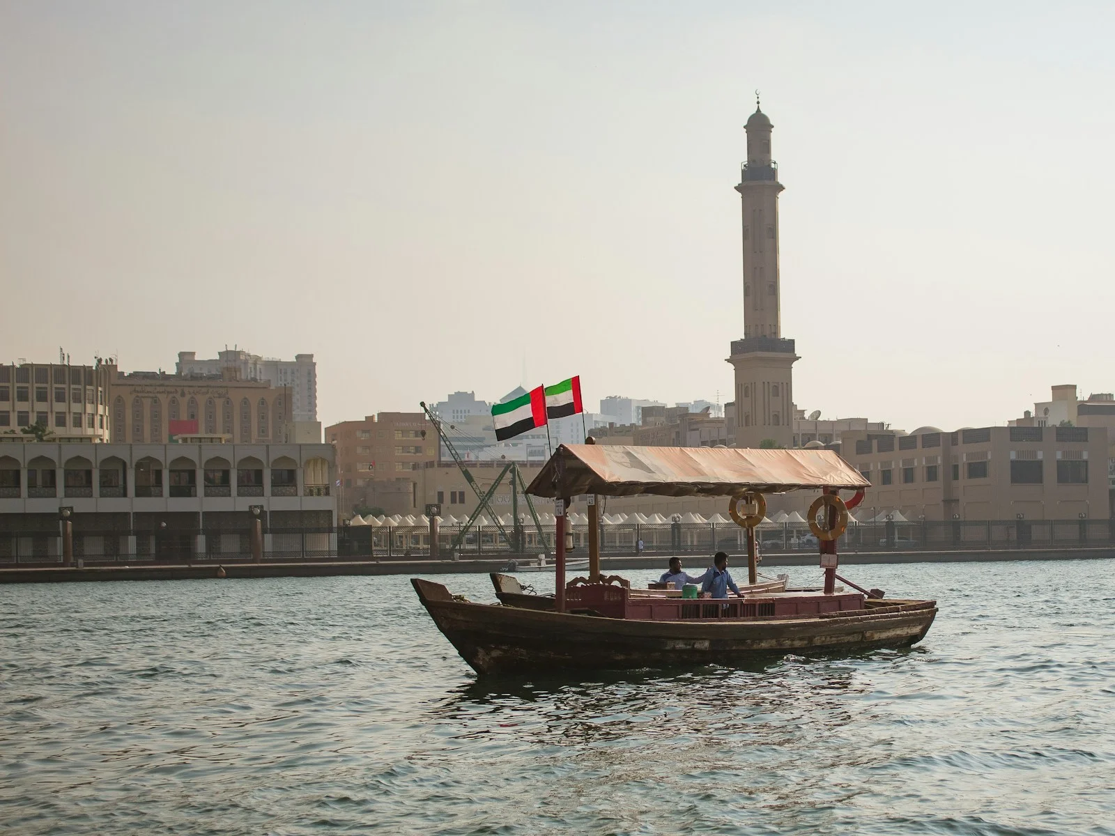 عبرة ترفع علم الإمارات في خور دبي، مع مئذنة على الضفة المقابلة