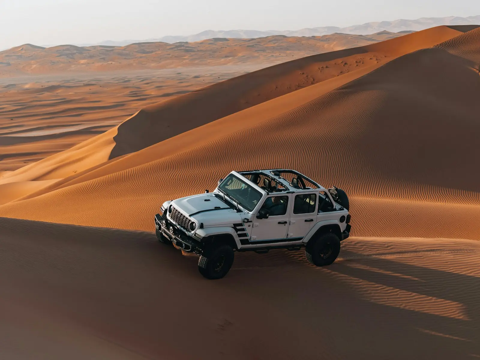 سيارة دفع رباعي (4x4) بيضاء على قمة كثيب رملي في صحراء خارج دبي، في ضوء أواخر النهار