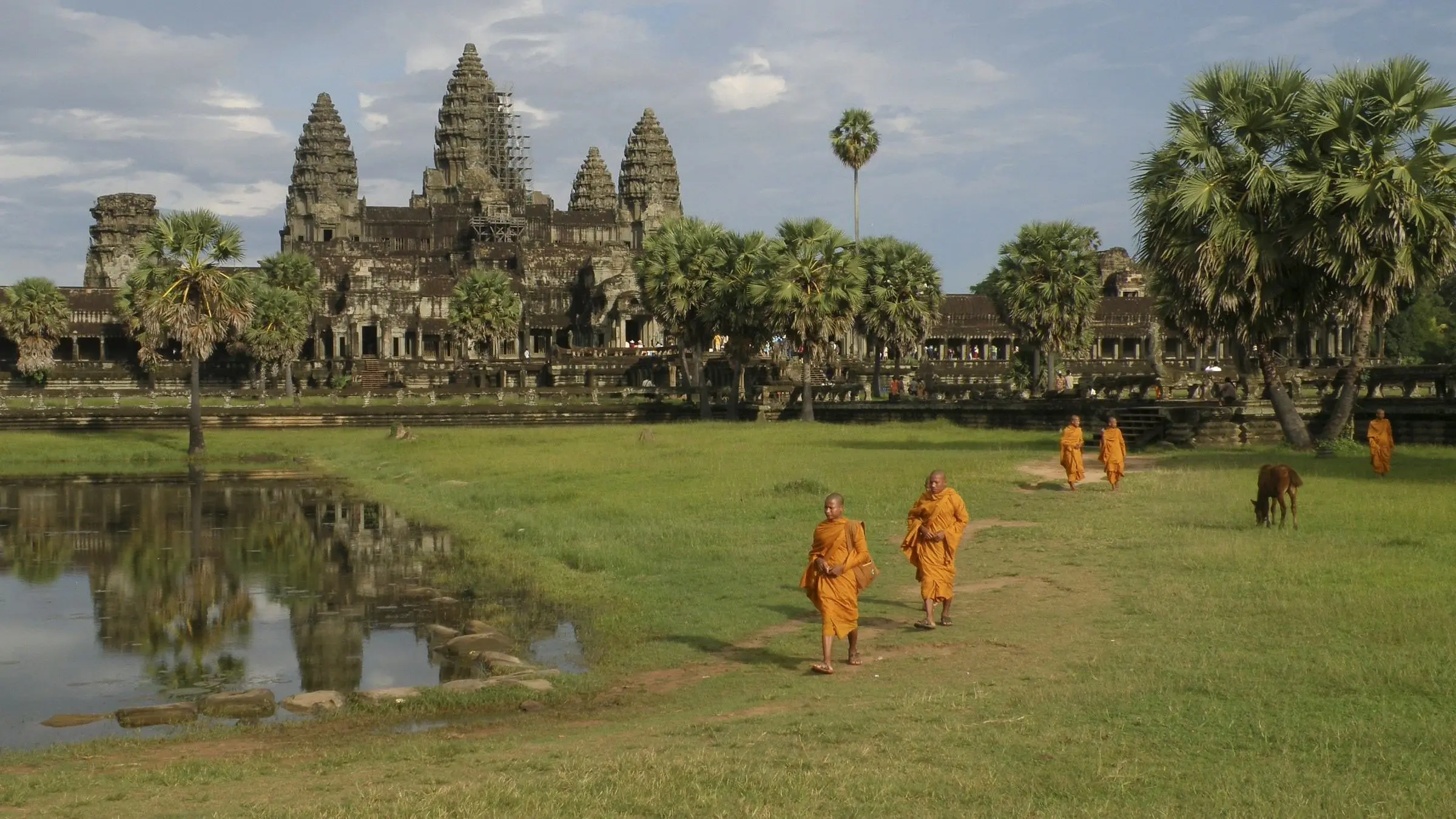 Monks in saffron robes cross the grass in front of Angkor Wat, near Siem Reap