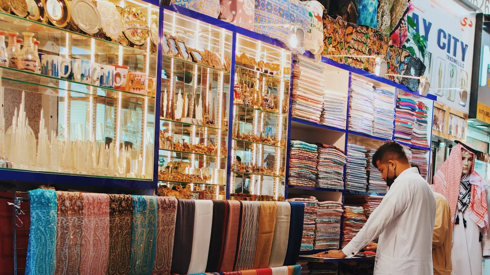 A shopper browsing rows of folded textiles and scarves at a souk stall