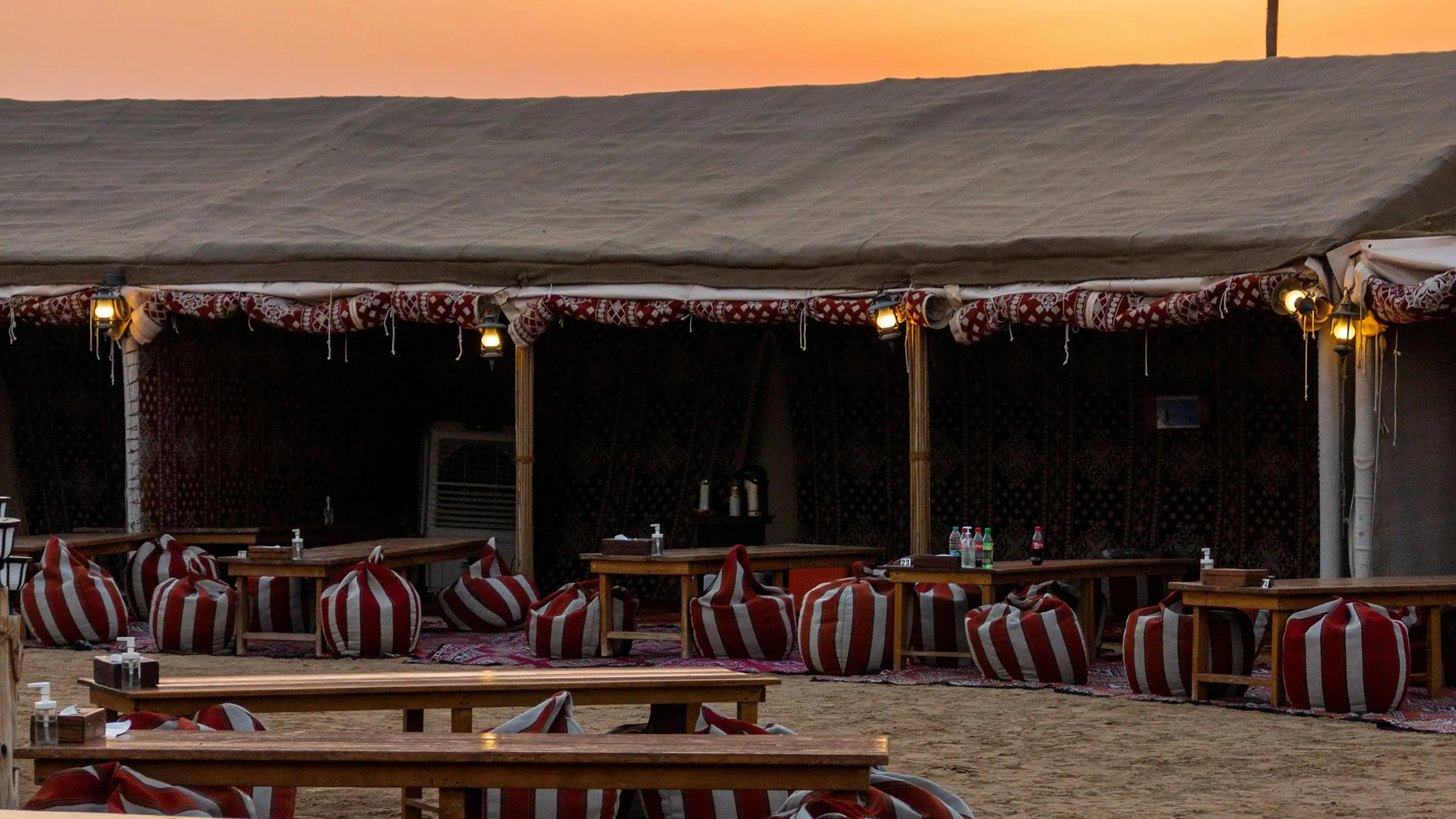 A desert camp near Dubai at sunset, laid out with low tables and majlis seating for a group