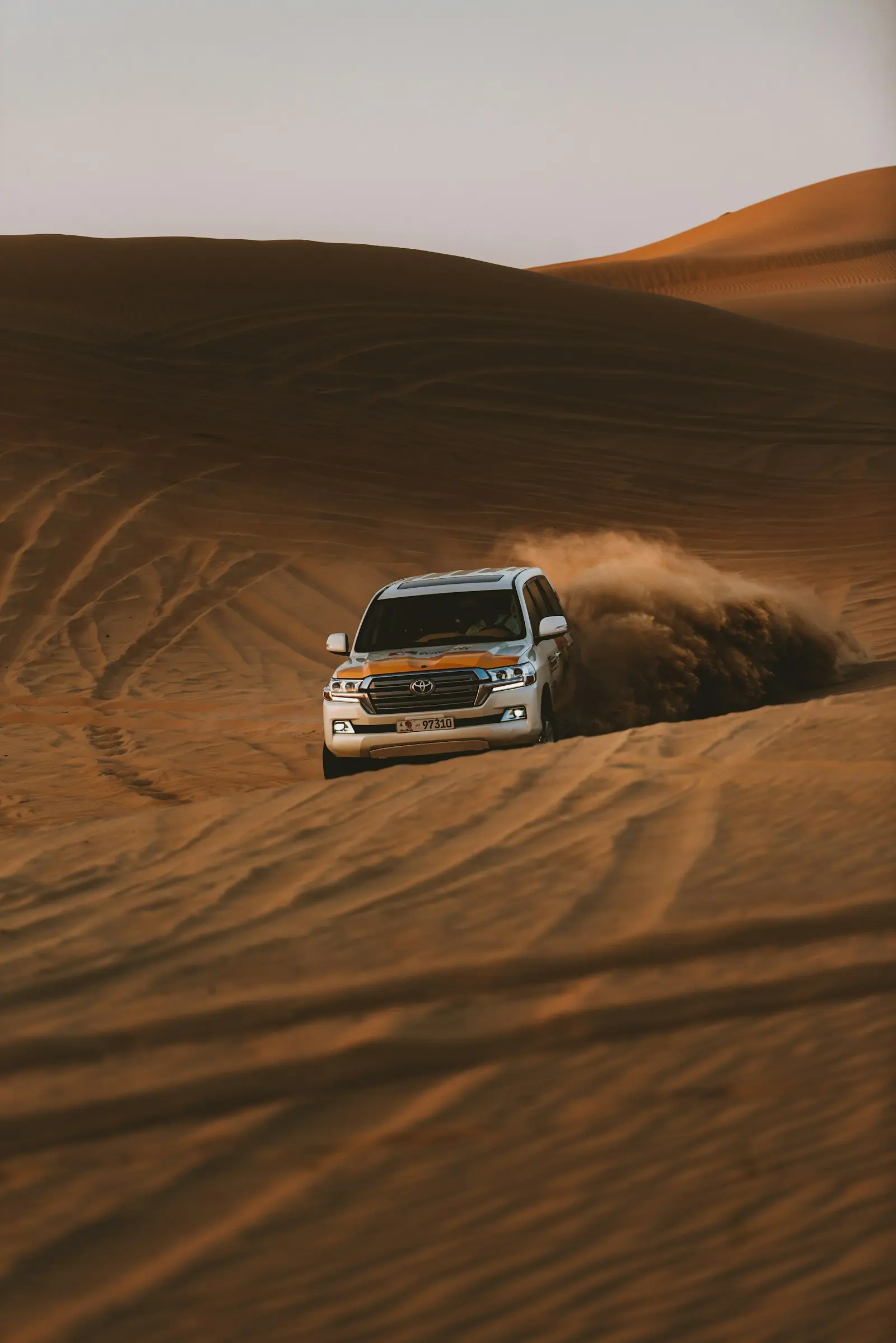 سيارة دفع رباعي (4x4) بيضاء تثير الرمال وهي تعبر كثيبا