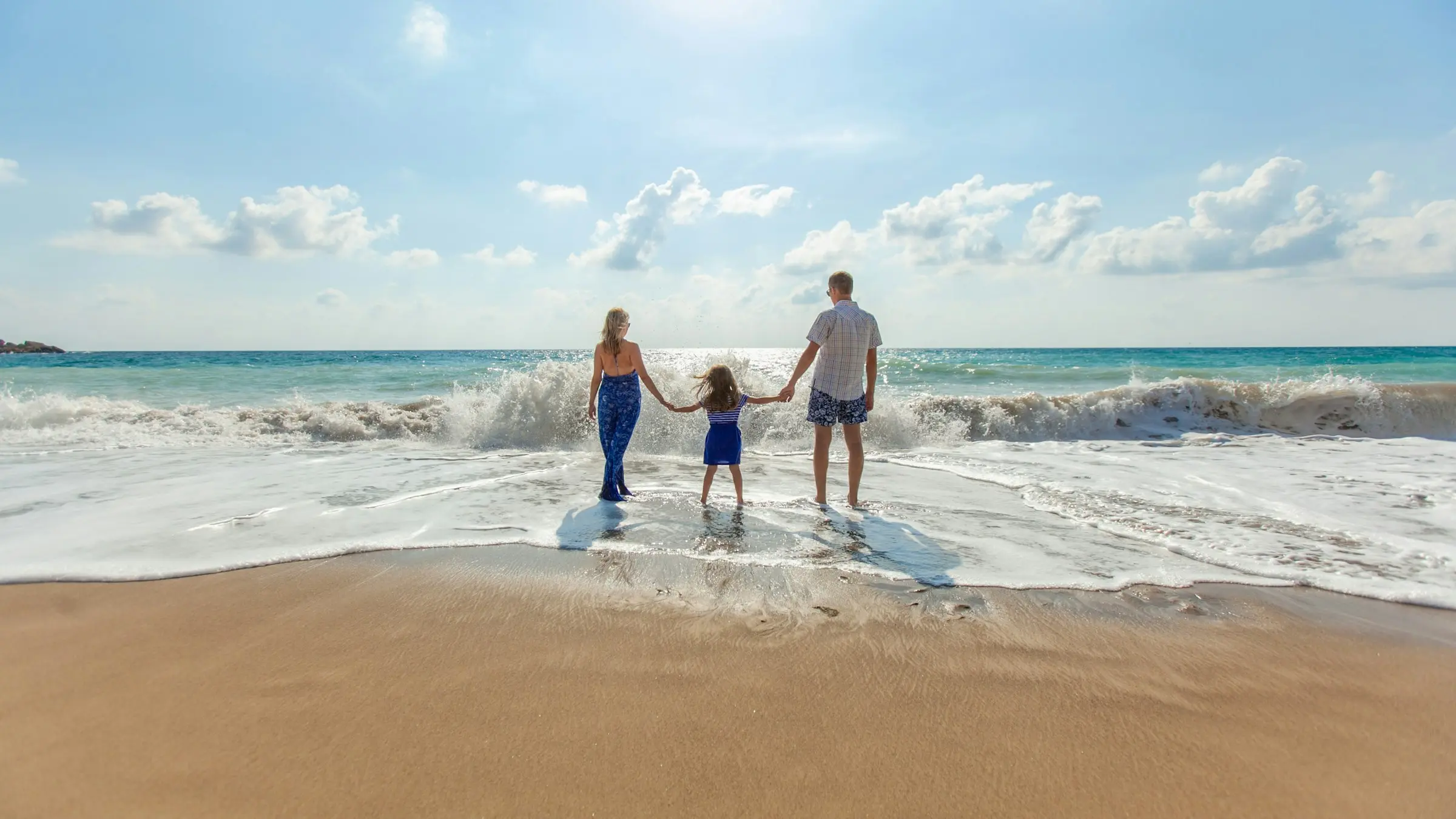 A family of three holding hands in the surf on a sunny beach