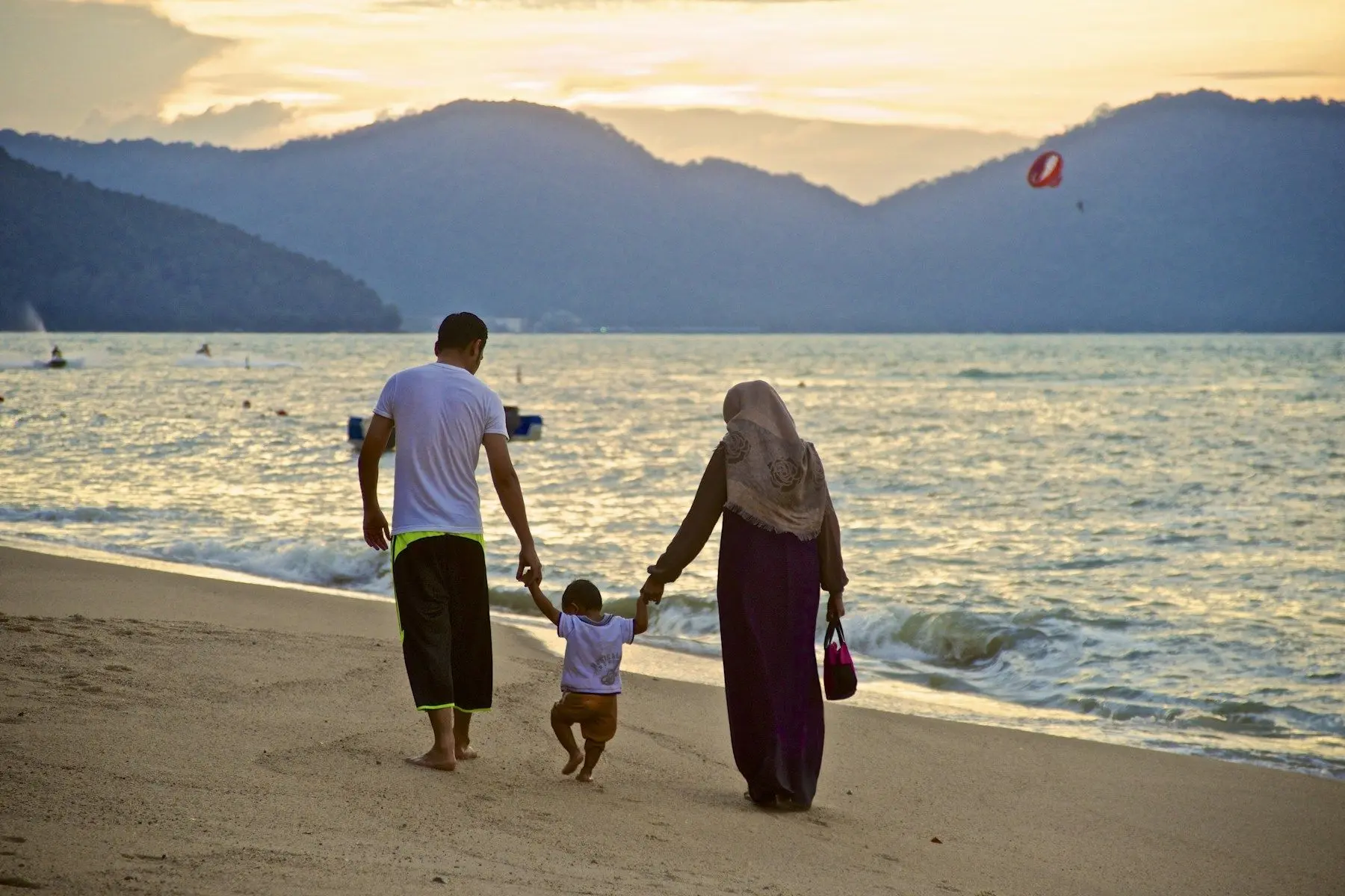 A couple walking a toddler along a UAE beach with mountains behind