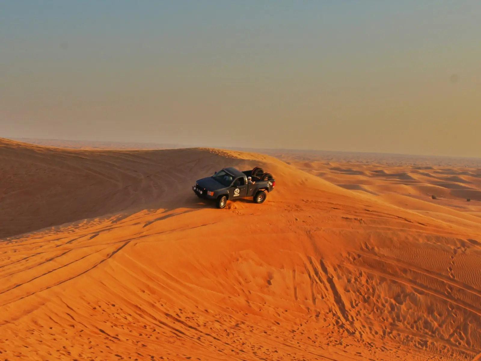 سيارة دفع رباعي (4x4) على حافة كثيب في صحراء دبي عند الغروب