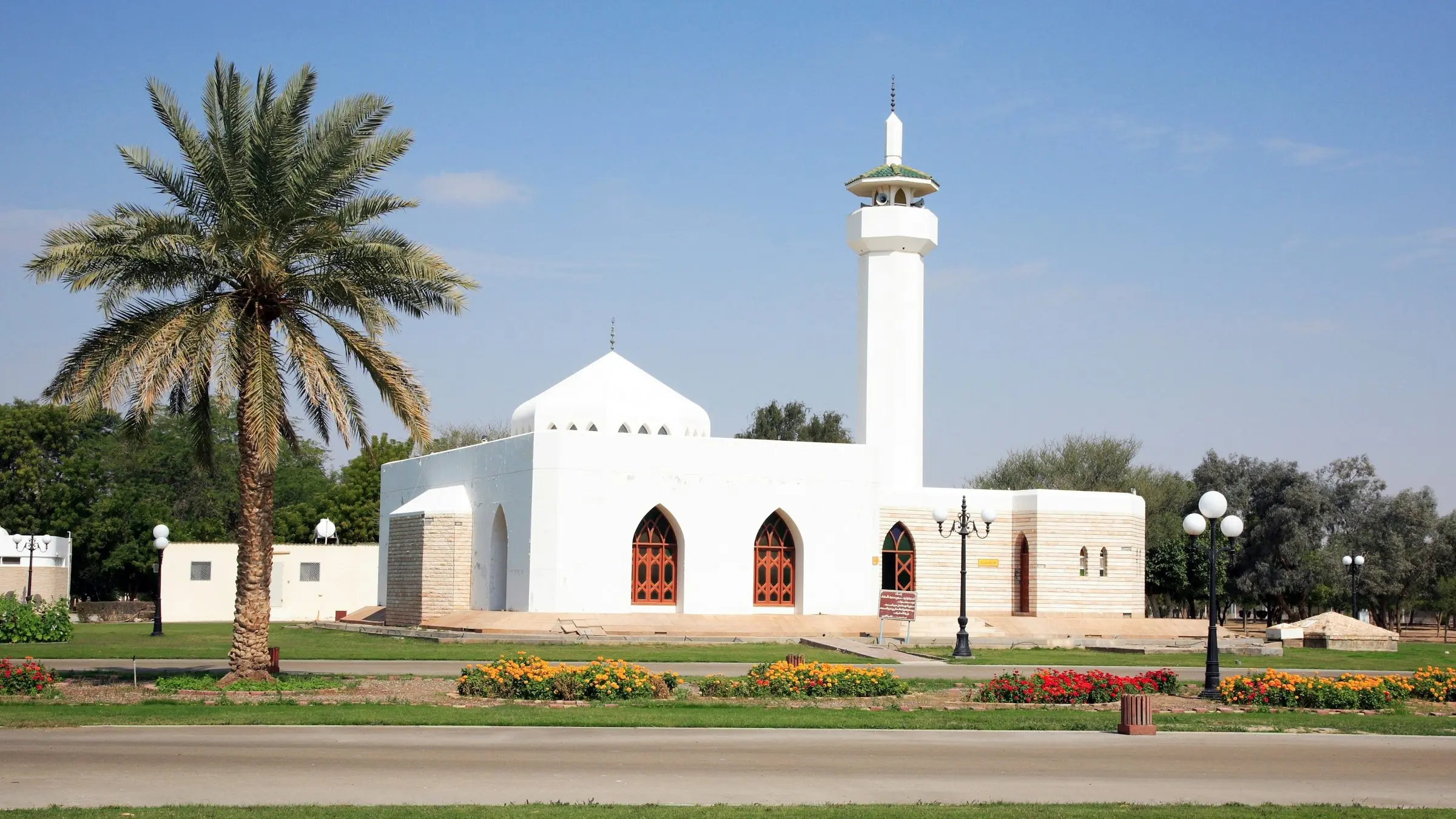 A white mosque among palms and flower beds in a park in Sharjah