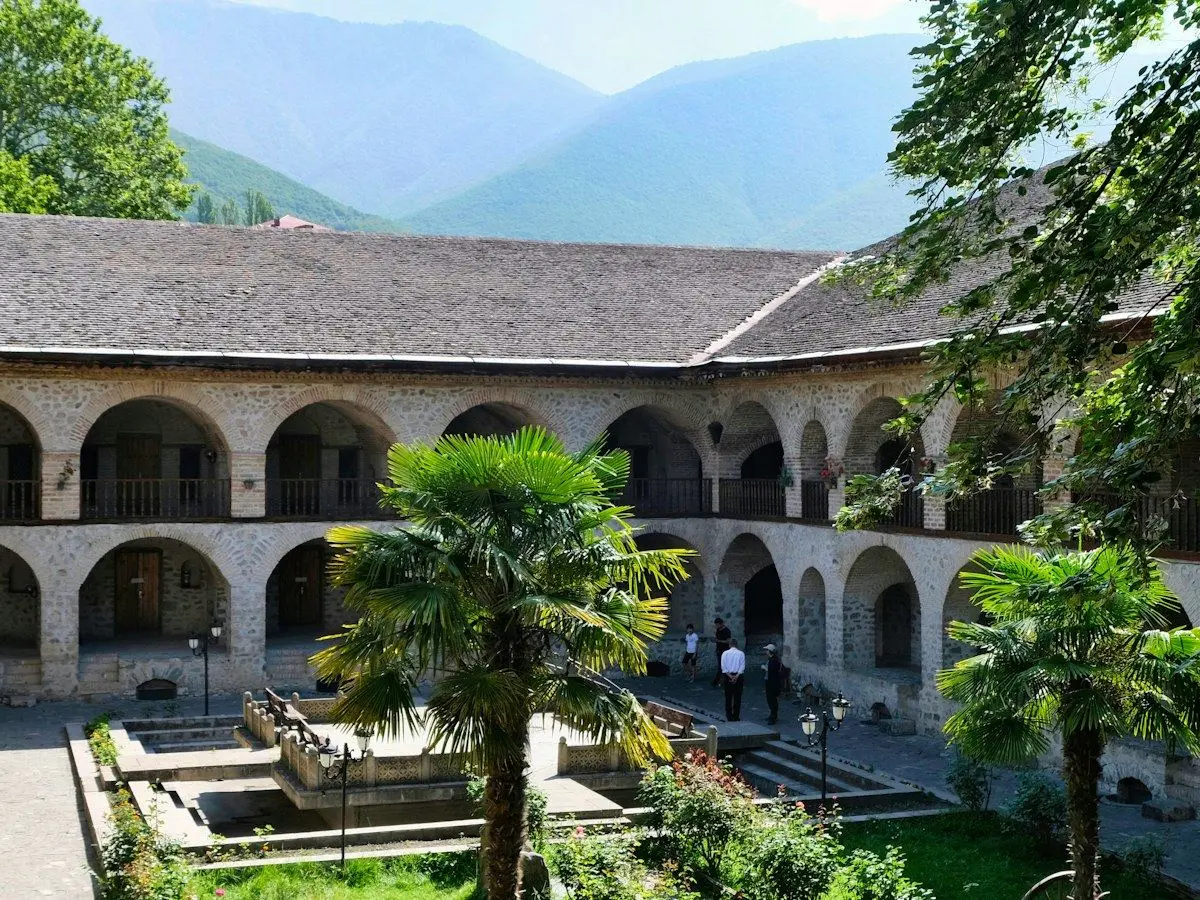 The arcaded courtyard of a caravanserai in Sheki below wooded mountains