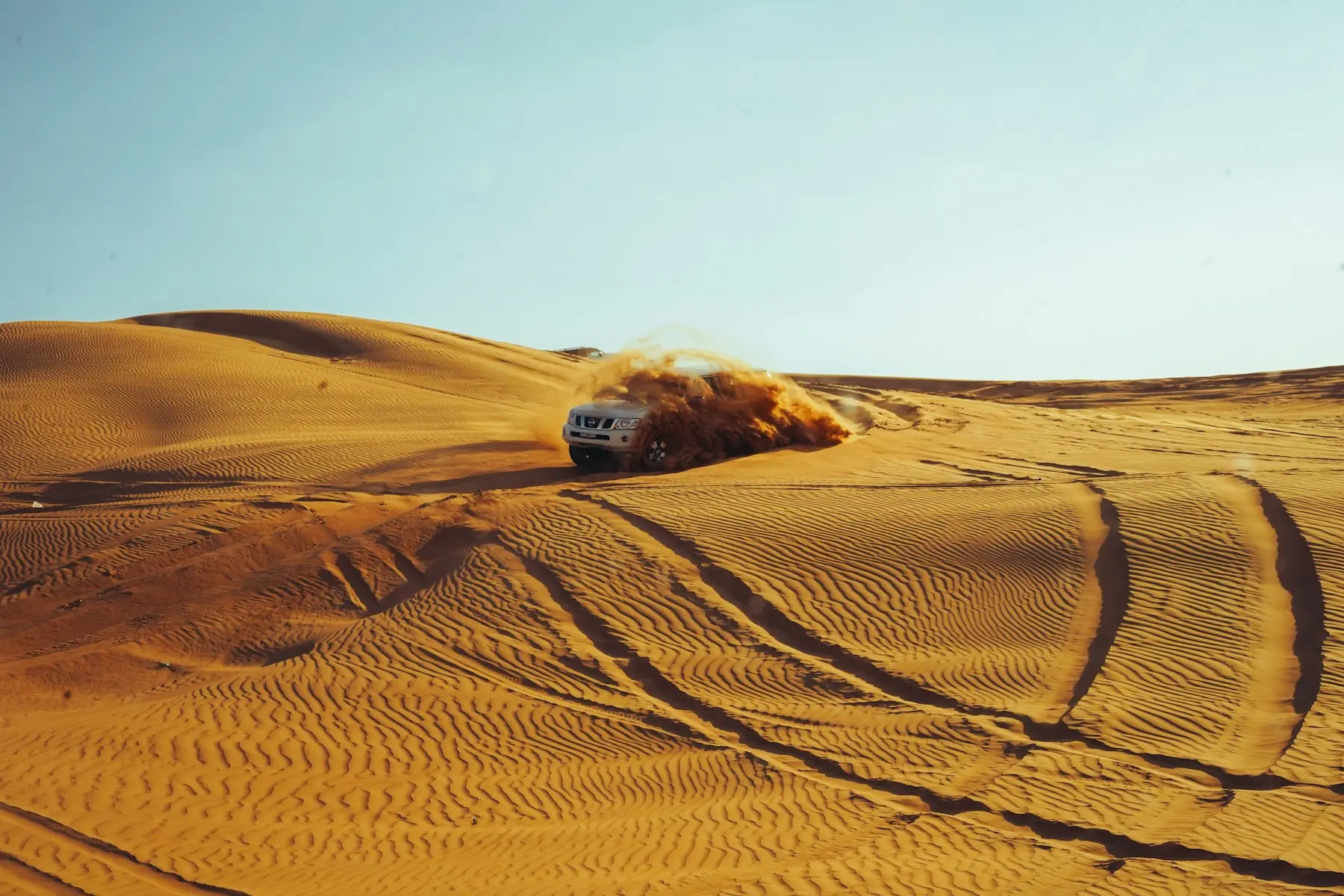 A 4x4 throwing up sand as it crests a dune on a Dubai desert safari