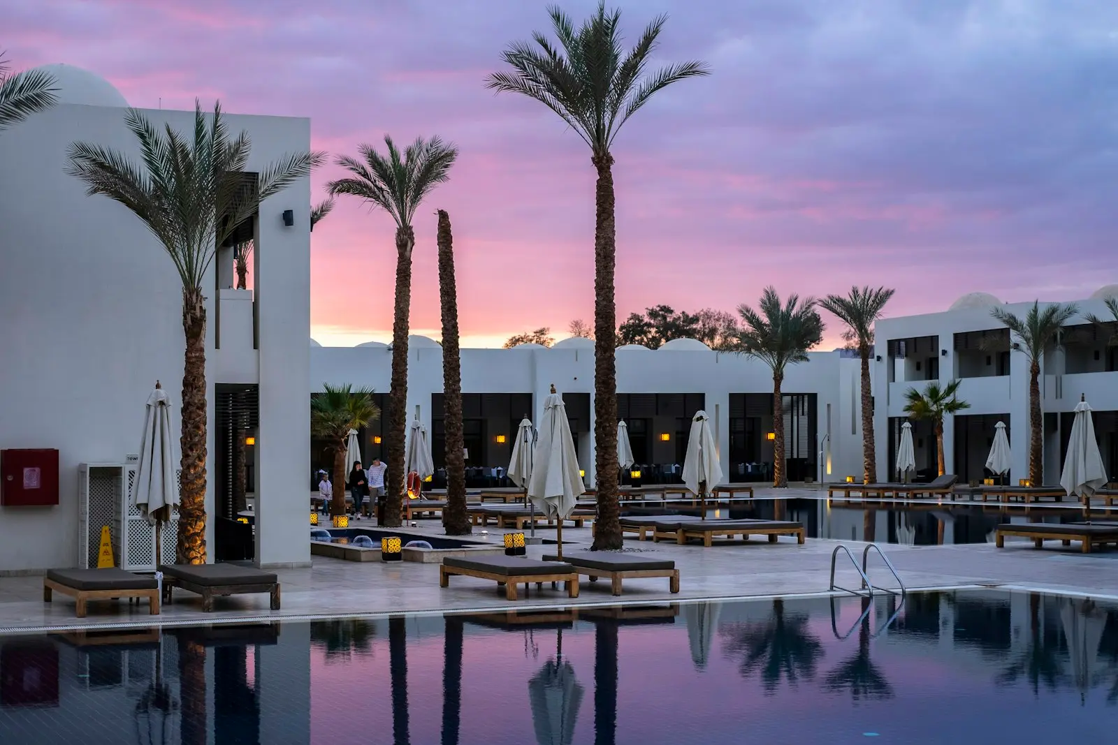 A palm-lined hotel pool at dusk