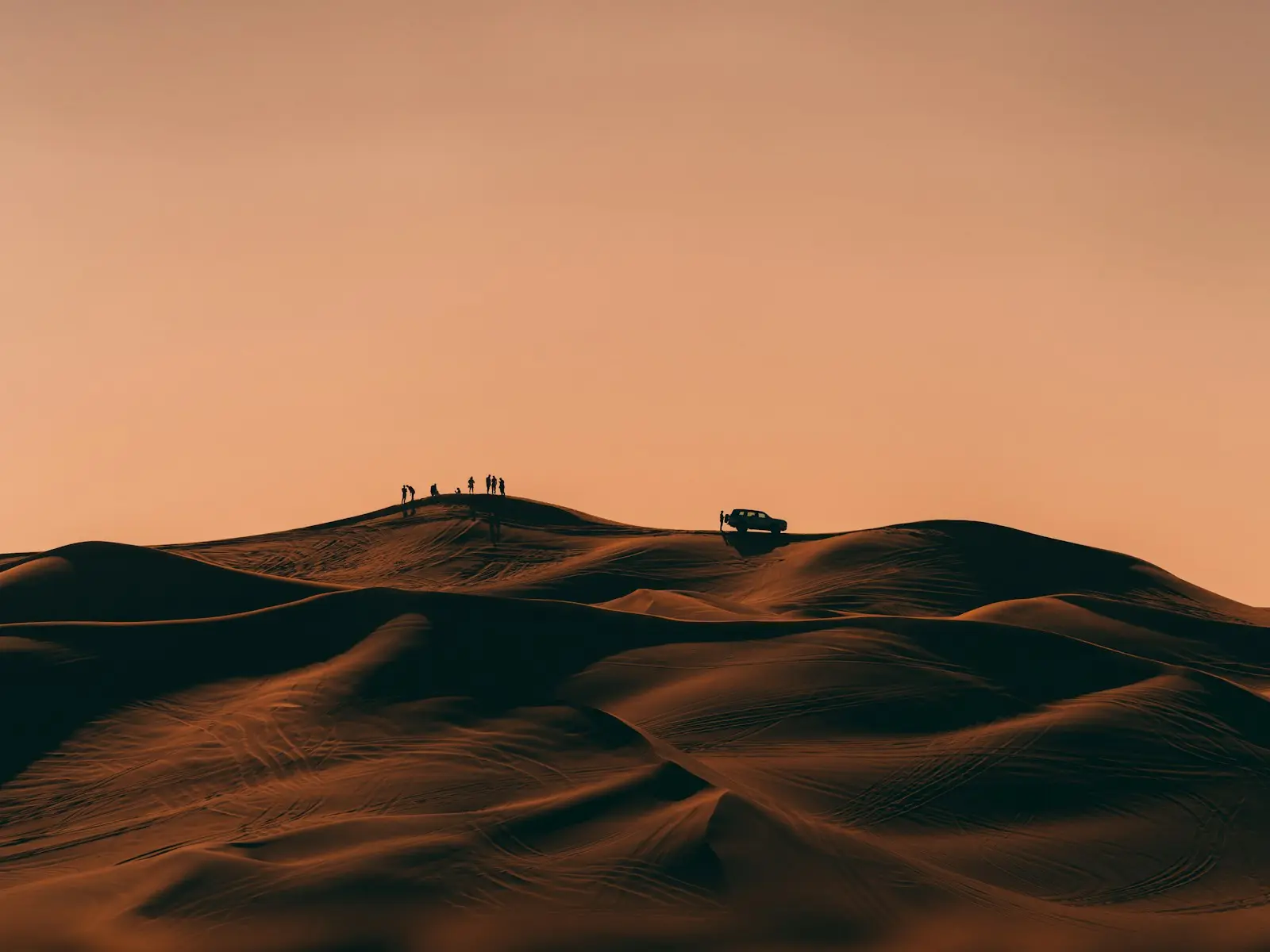 أشخاص يمشون على قمة كثيب رملي عند الغروب في الصحراء خارج دبي