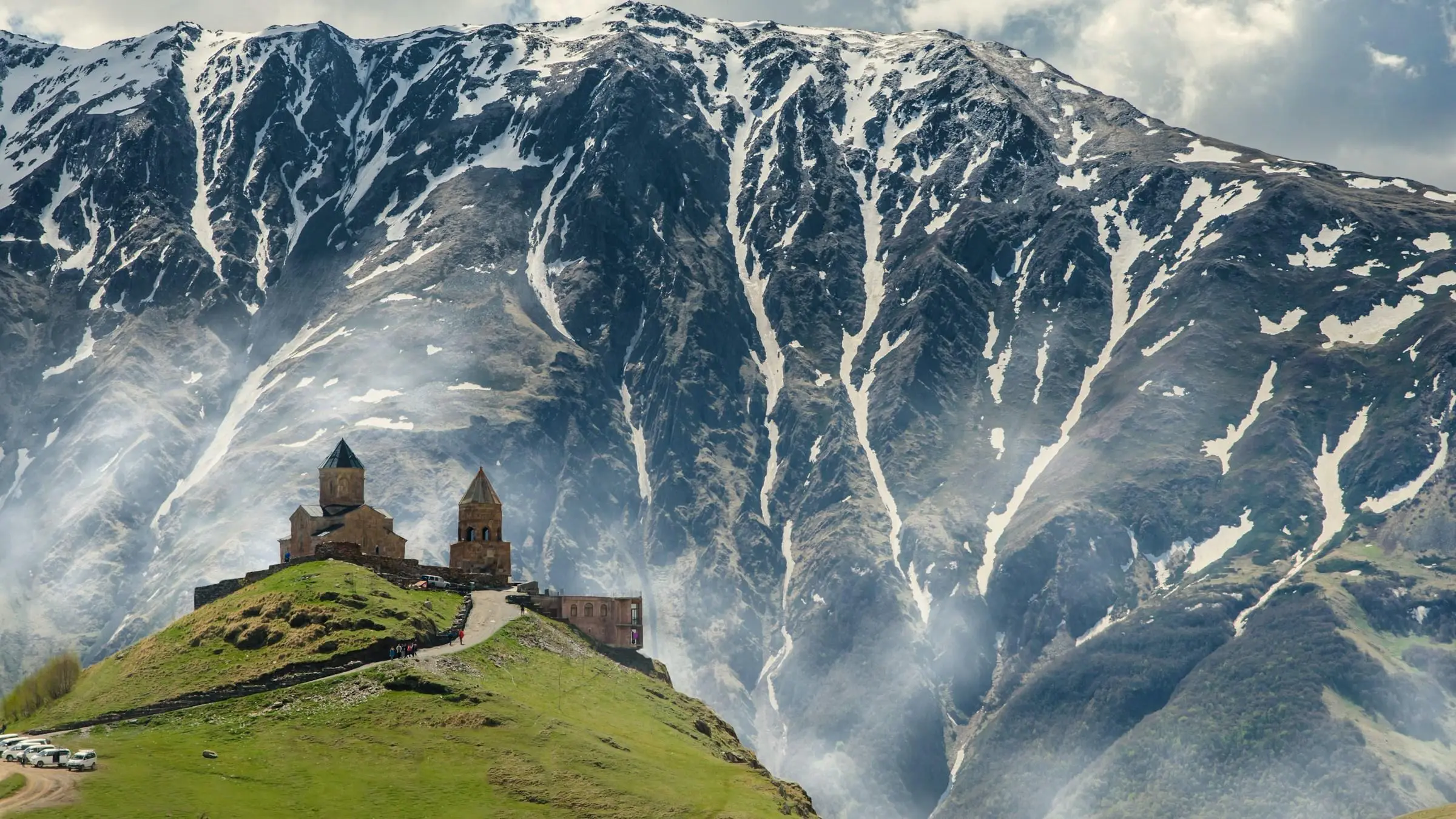 Gergeti Trinity Church on its hill above Stepantsminda, with snowy Caucasus slopes behind