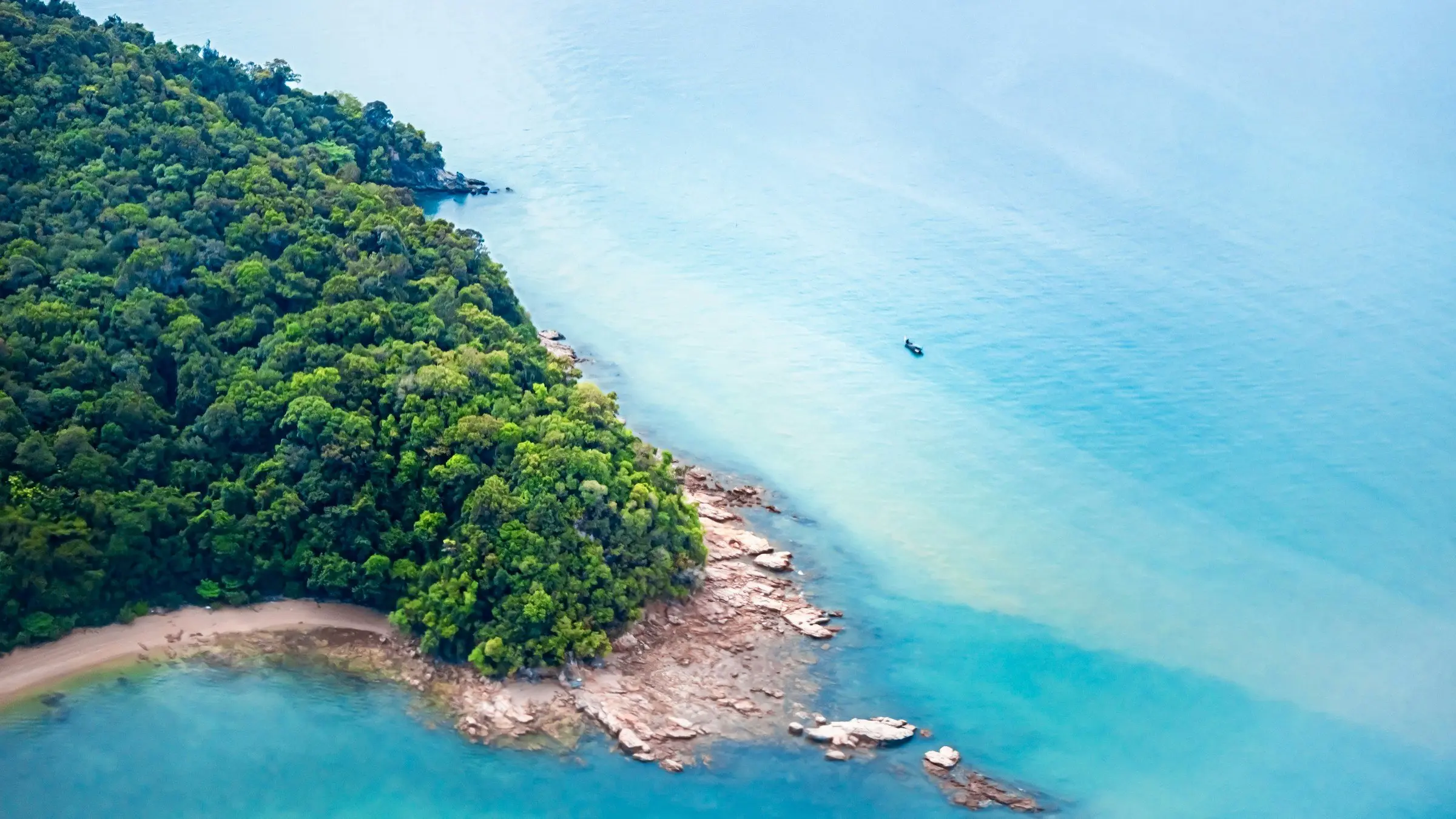 A forested headland and clear shallow water off Langkawi, Malaysia, seen from above