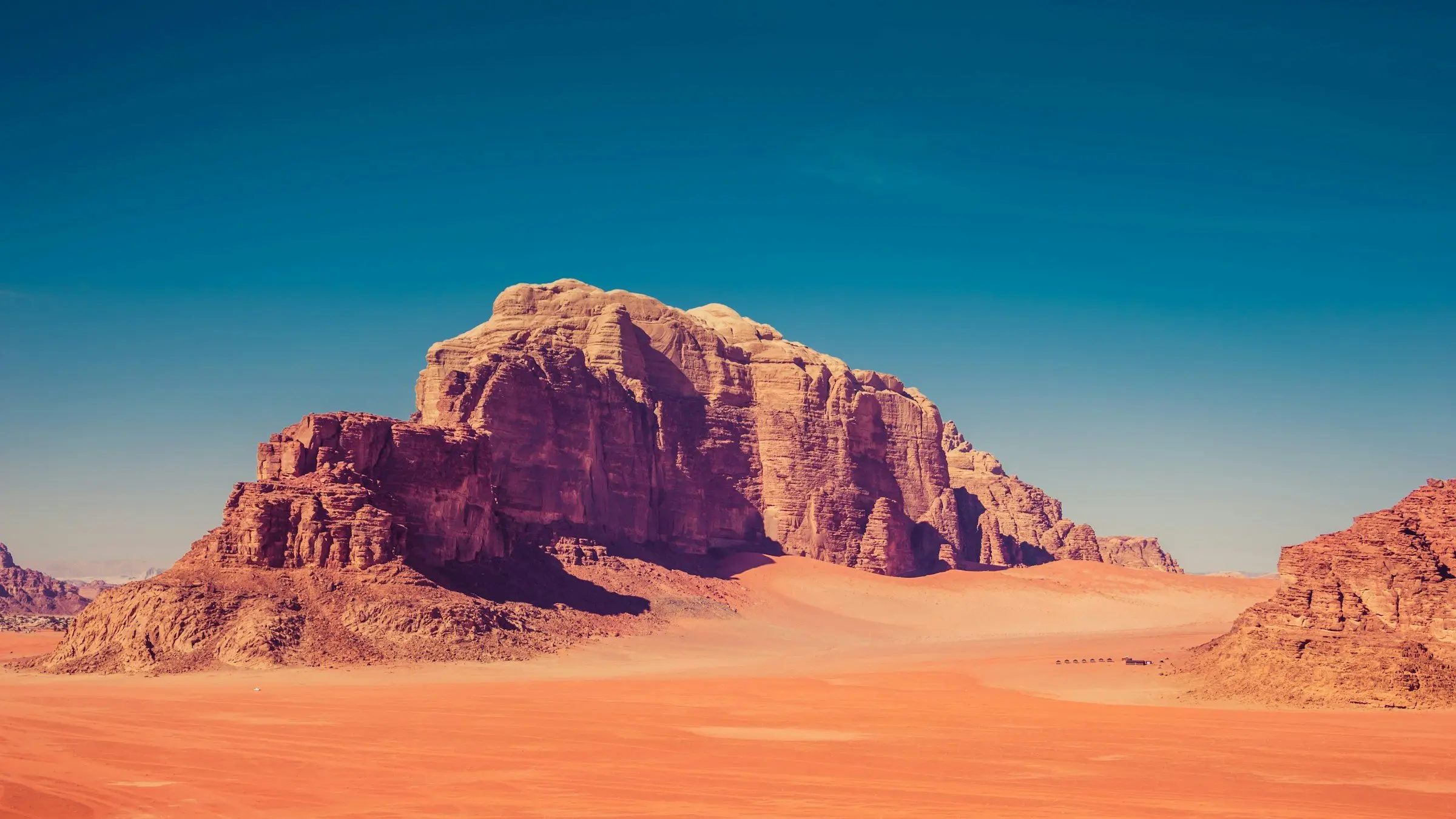 A sandstone massif rising from red sand in Wadi Rum, Jordan